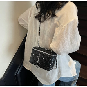 Detail of black quilted chain bag with silver studs and rose pendant worn on back