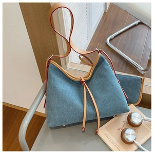Detailed view of blue denim tote bag with brown leather straps and metal base studs