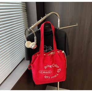 Detail of red drawstring canvas tote bag with white circular text print and wide strap