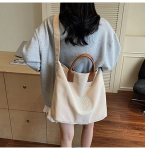 Détail du sac cabas en toile blanc cassé avec anses en cuir marron et lettrage graphique bleu