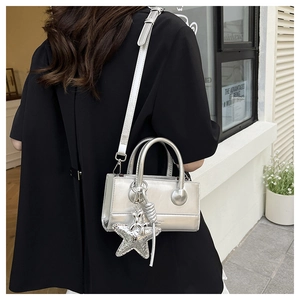 Silver mirror finish crossbody bag with star charm and chain strap detail on model