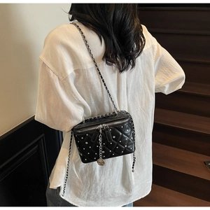 Detail of black quilted chain bag with rhinestone accents and camellia pendant on a model