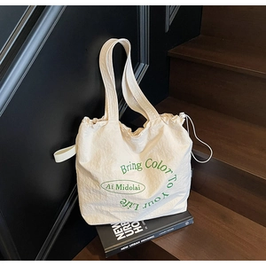 Detail of off-white canvas tote bag featuring green lettering and drawstring closure