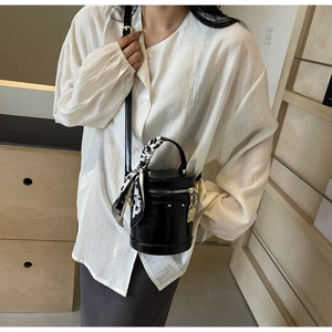 Detail of a black cylinder bucket bag with a patterned scarf handle and gold lock charm