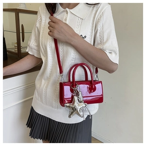 Detail of red patent leather crossbody bag featuring a silver star charm and strap