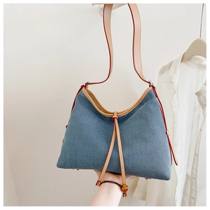 Detail of blue denim tote bag with brown leather trim and decorative strap accents
