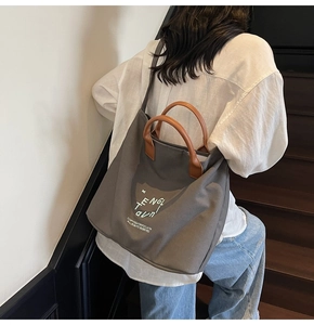 Detailed view of grey canvas tote bag with brown leather handles worn by a model