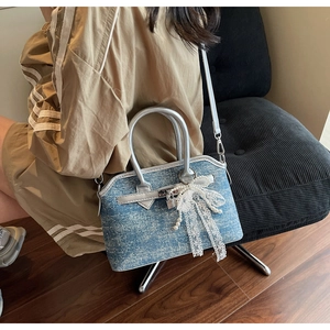 Détail du sac bandoulière en denim bleu avec garniture en cuir argenté et nœud