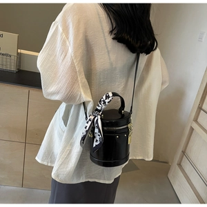 Close-up of black bucket bag with silk scarf on handle and golden metal padlock detail