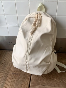 Minimalist beige nylon backpack with woven zipper pulls and drawstring side pockets