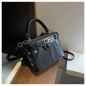 Close-up of black retro box-shaped handbag with golden hardware and textured stitching