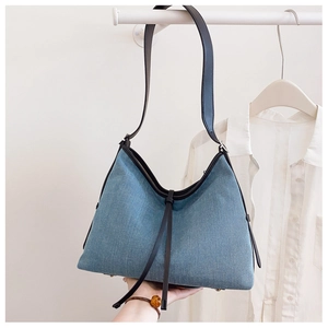 Detail of light blue denim tote bag featuring black leather trim and bottom metal studs