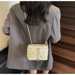 Detail of off-white quilted crossbody bag with silver rivets and metal chain strap