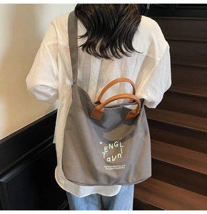 Sac fourre-tout en toile grise avec anses en cuir marron porté à l'épaule dans un escalier