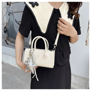 Detail of glossy cream small square bag featuring a bold silver star pendant accessory