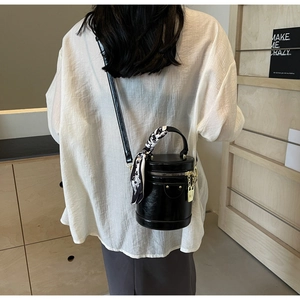 Back view of a model carrying a black glossy cylinder bag with decorative silk scarf