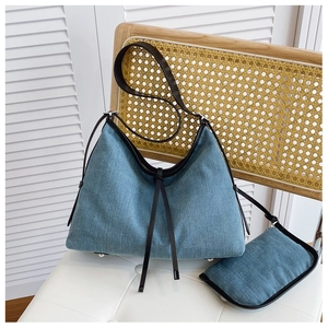 Detail of blue denim hobo bag featuring leather trim on a vintage wicker chair