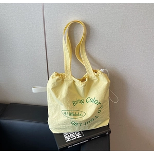 Detail of light yellow canvas tote bag with green lettering on a black leather sofa