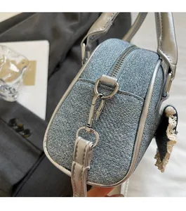 Close-up of blue denim shell bag showing silver metal zippers and lace charm detail