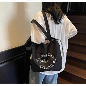 Close-up of black canvas drawstring tote bag with white slogan worn by a model