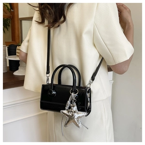 Detail of glossy black leather crossbody bag with silver star charm and round handle grip