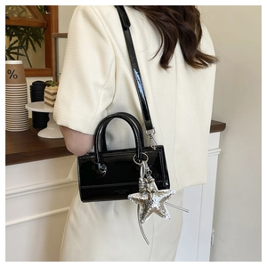 Detail of black patent leather crossbody bag with a large silver starfish pendant