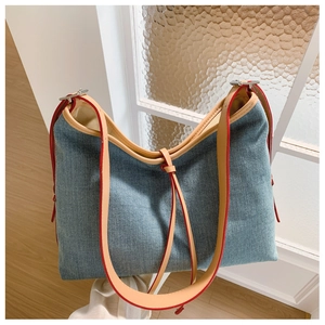 Detailed view of blue denim tote bag featuring brown leather straps and red painted edges