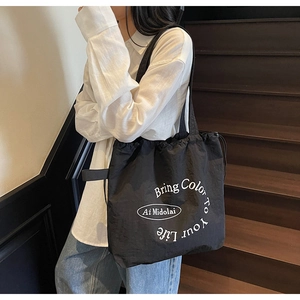 Detail of black nylon tote bag with drawstring closure and artistic white text print