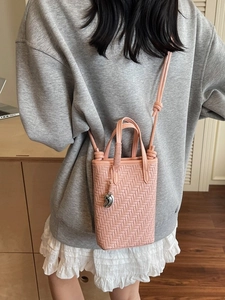 Petit sac seau tressé rose avec bandoulière et pendentif sur une tenue décontractée