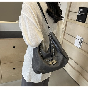 Detail der grauen Denim-Hobo-Tasche mit Metallkette und Lederriemen an einem Modell