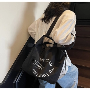 Detail of a black canvas tote bag showing the wide shoulder strap and printed lettering