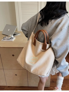 Grand sac cabas en toile blanc cassé avec anses en cuir marron porté par un mannequin chic