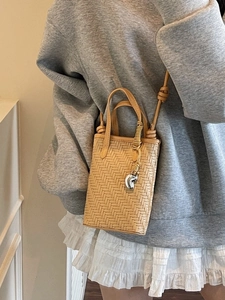 Petit sac seau tressé beige à la mode avec breloque argentée porté à l'épaule