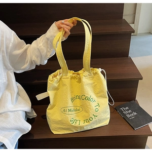 Detail of light yellow pleated canvas tote bag with drawstring and printed slogan