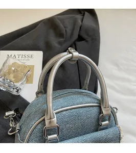 Close-up of blue denim shell bag featuring silver metallic handles and zipper detail