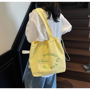 Detail of yellow drawstring canvas tote bag with green lettering and adjustable strap