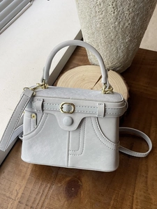 Light gray mini box bag with denim-style stitching and gold metal hardware on wooden table