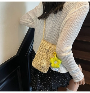 Dettaglio della borsa a tracolla in paglia intrecciata beige con ciondolo floreale