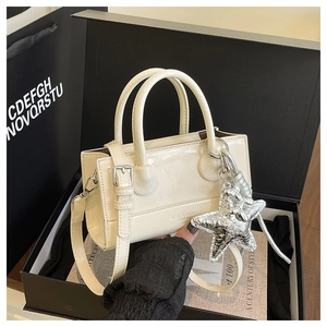 Detail of cream patent leather bag with silver star charm and cylindrical handles