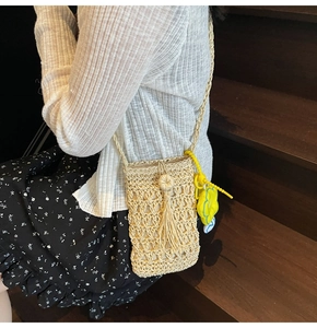 Dettaglio della borsa a tracolla in paglia fatta a mano con nappa a frange e ciondolo a fiore