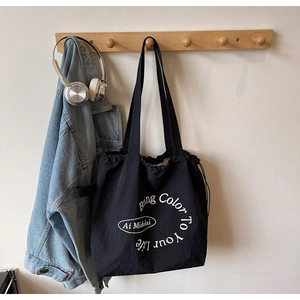 Detail of black drawstring tote bag with white text hanging on hook with headphones