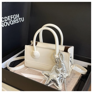 Close-up of a cream patent leather crossbody bag with silver star charm in a gift box