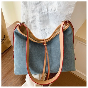 Detail of light blue denim tote bag with brown leather straps and red painted edges