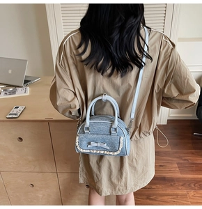Detail of light blue denim shell bag with bow decoration and lace trim worn by a model