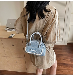 Detail of light blue denim shell bag with lace trim and bow worn in a home setting