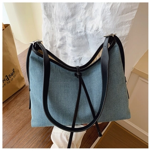 Detail of blue denim tote bag featuring black leather straps and textured fabric finish