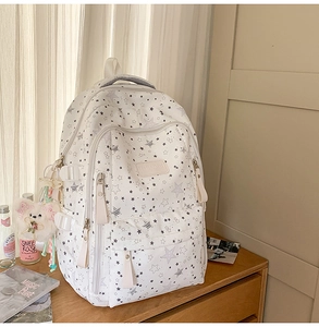 Detail of white star pattern backpack featuring multiple compartments and a plush bear charm