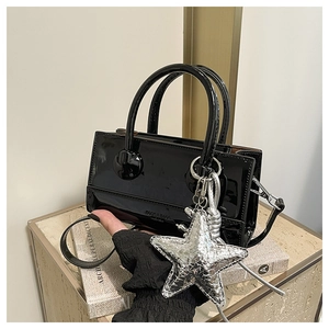 Detail of glossy black KOSKA handbag with silver star charm and metallic top handles