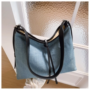 Detail of light blue denim hobo bag with adjustable black leather shoulder strap and metal buckle