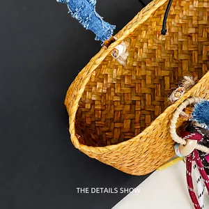 Detail of hand-woven straw beach bag featuring denim handles and bohemian tassels
